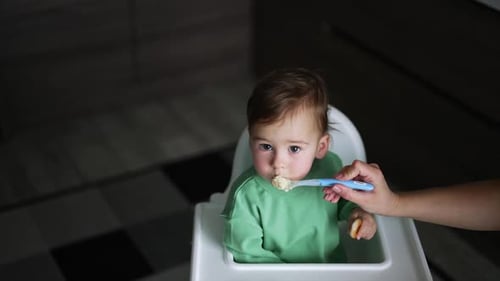 Nourishing the little toddler sitting in the feeding table. High angle view.