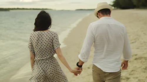 Young Couple Holding Hands and Walking Down the Beach Close to The