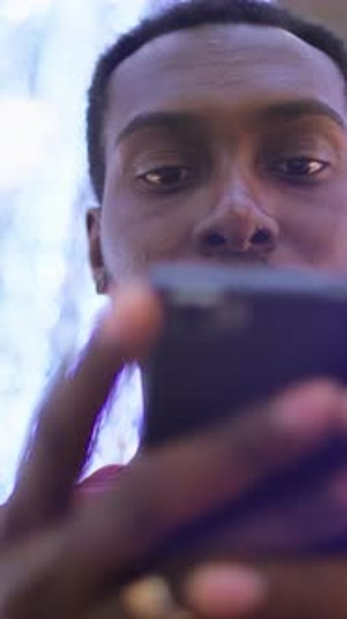 Homme afro-américain concentré sur un smartphone dans un environnement lumineux avec des lumières floues en arrière-plan