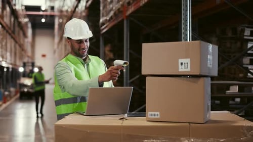 Male Worker Scanning Box with Barcode Scanner Using Laptop at Warehouse