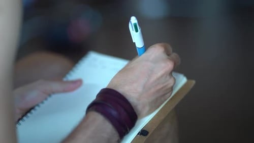 Caucasian Male Writing with Right Hand on a White Note Book with Multi Color Pen.