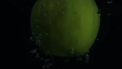 Real time shot of falling green apple in water with bubbles in front of black blackground