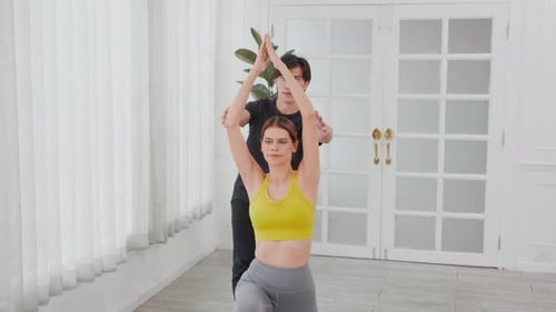 Junger asiatischer Trainermann trainiert Frau beim Yoga, während er die Hände streckt und im Raum balanciert.