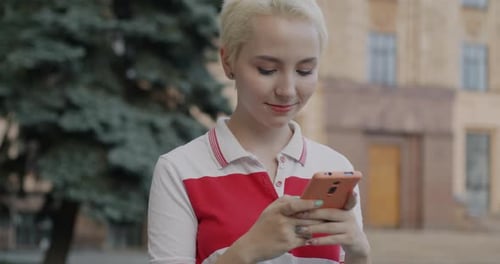 Slow Motion Portrait of Cheerful Young Lady Using Smartphone and Laughing Standing in Street