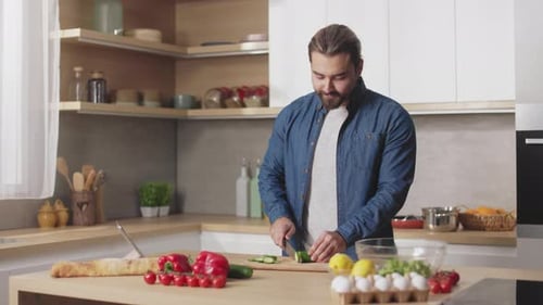 Man Cutting Vegetables and Looking on Tablet Screen at Home
