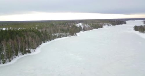Aerial, idyllic isolated rural village surrounded by endless pine and spruce forests and frozen lake