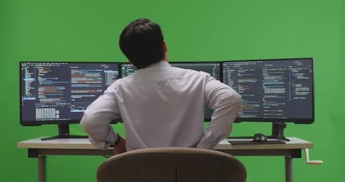 Back View Of Developer Having Backache While Write Code With Multiple Screens In Green Screen Studio