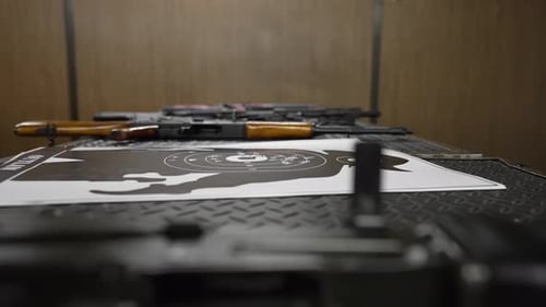 Seitenansicht von Waffen und einer gebrauchten Zielscheibe mit Löchern, die auf einem Tisch an einem Schießstand liegen