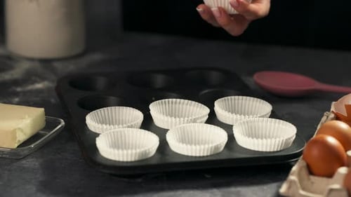 Person placing cupcake liners into tray on table, static medium shot, slow motion