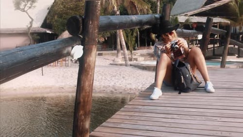 Blonde woman sits on dock with camera smiling