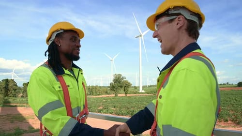 Smart engineers with protective helmet shaking hands at electrical turbines field