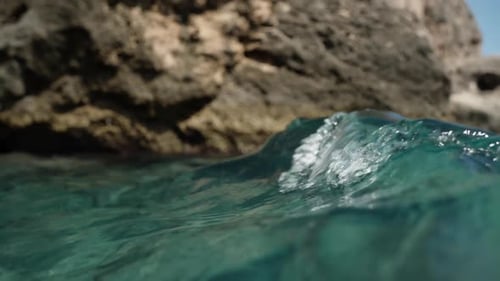 The camera sways at the water's edge on the turquoise ocean waves, with the backdrop of cliffs.