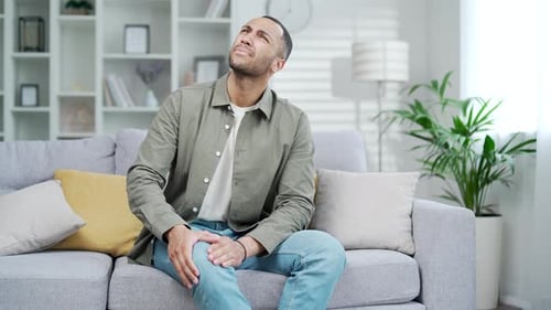 Young Man Massaging Sore Knee in Living Room
