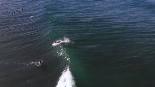 Surfer riding a wave while it is crashing in the blue ocean from a drone during a clear day with blu