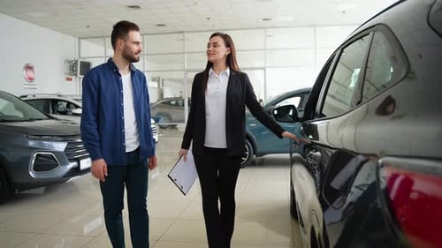 Female Car Dealer Showing New Car to Customer in Showroom