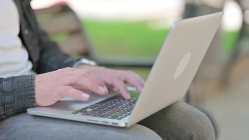 Nahaufnahme einer männlichen Hand, die auf einem Laptop im Freien tippt