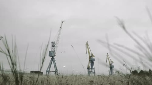 Wir nähern uns großen Kränen über einem Grasfeld in der Tiefe