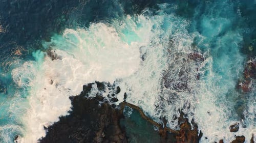 Azure Ocean Waves Roll Crashing at Rocky Shore Volcanic Formations with Splashing and White Foam