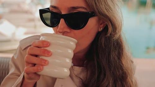 Woman Drinks Coffee Outdoors Wearing Sunglasses and Coat