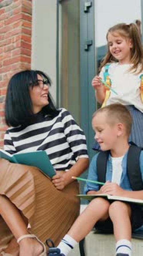 Attentive School Small Children and Woman Sitting in Circle on Stairs of School Building Background
