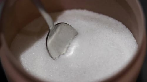 Spoon Scooping White Granulated Sugar from Bowl