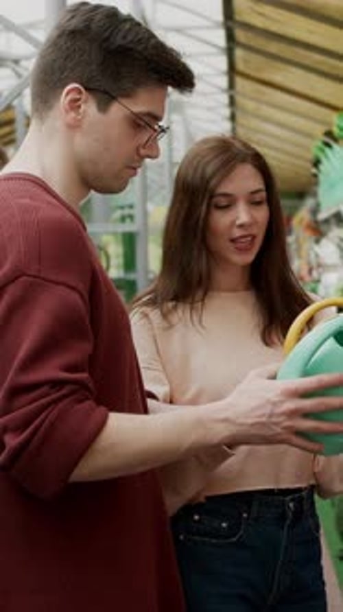 Focused Brunette Woman with Her Boyfriend Choosing the Color of a Watering Can in a Garden and