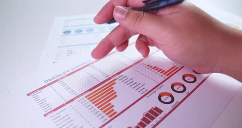 Close-up of businessman's hands with pen working at office desk and analyzing dashboard graphs and c