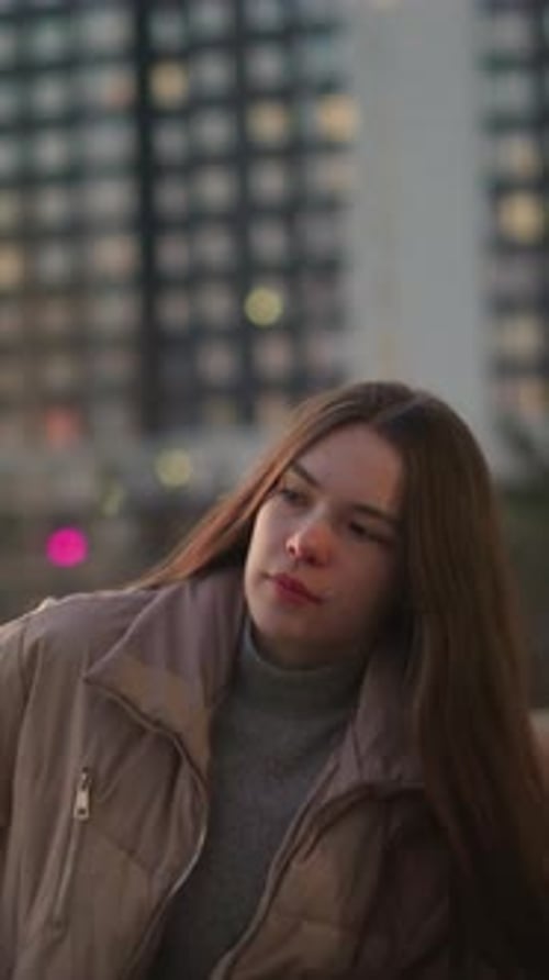 Young Woman in Urban Park Sitting on Bench and Gazing Off Thoughtfully