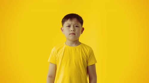 Boy Shrugs with Uncertainty in Front of Yellow Background