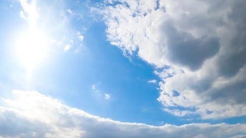 Strahlende Sonne am blauen Sommerhimmel. Eine große graue Wolke nähert sich, um die Sonne zu verbergen. Ansicht von unten.