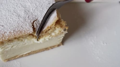 Fork Cutting a Cream Cake with Powdered Sugar