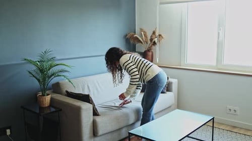 Woman arranging cushions on sofa in modern living room