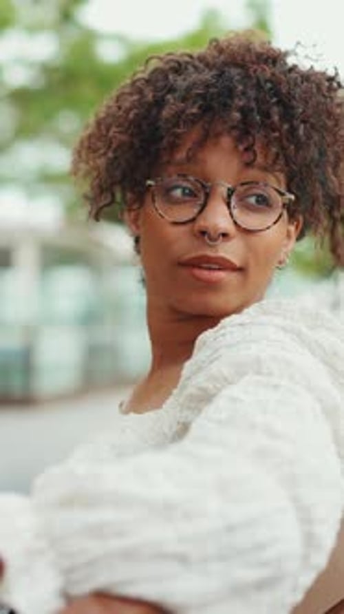 Close-up portrait of woman in glasses sits on a bench smiling and looking around