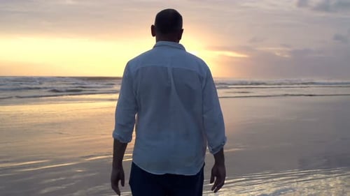 Junger Mann geht bei Sonnenuntergang am Strand spazieren Erwachsener