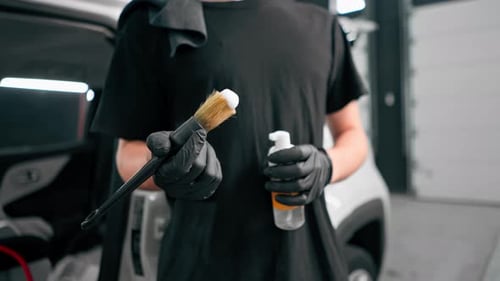 Close-up of a car wash worker using a plastic washing brush while cleaning the door card of a car