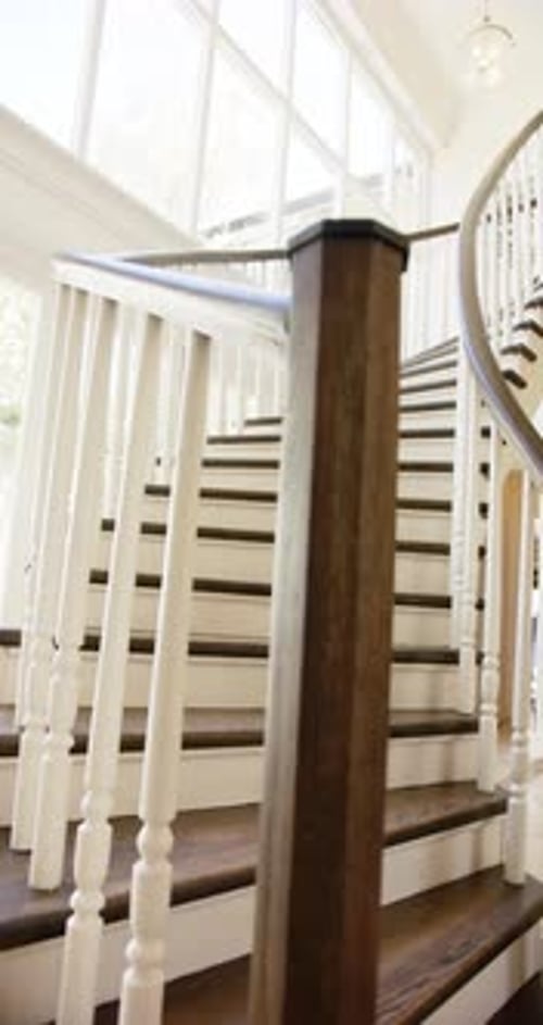 Vertical video: Curved staircase with wooden handrail in modern, bright home interior