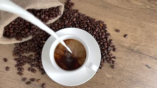Milk Pouring into Cup of Coffee Beans