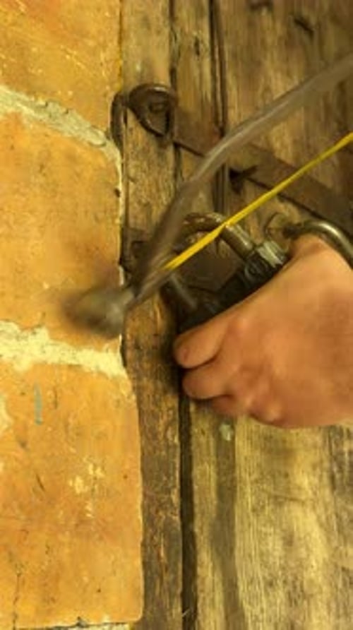 Man Cutting Padlock With Hacksaw. Vintage Wooden Door In Brick Wall. Close Up. Vertical Video.