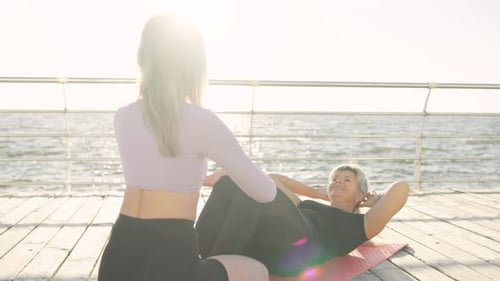 Under the Guidance of a Trainer a Senior Woman Trains Outdoors By the Ocean Pump Her Abs
