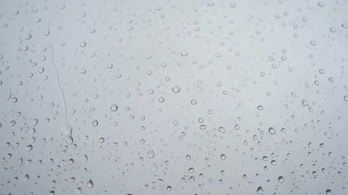A slow-motion close-up footage of heavy rain drops is seen through a window glass.