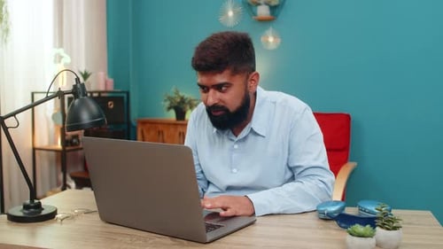Indian Man Rubs Forehead at Laptop Error Screen Sighs Distressed Virus Glitch Problem Indoors Table