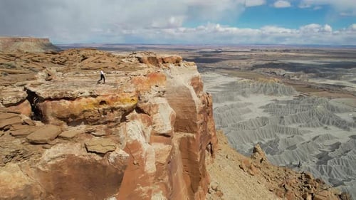 Aerial View of Young Woman Walking on Top of Mesa Near Cliff Above Desert Badlands, Drone Shot