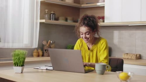 Young Woman Smiling and Laughing at Laptop in Kitchen