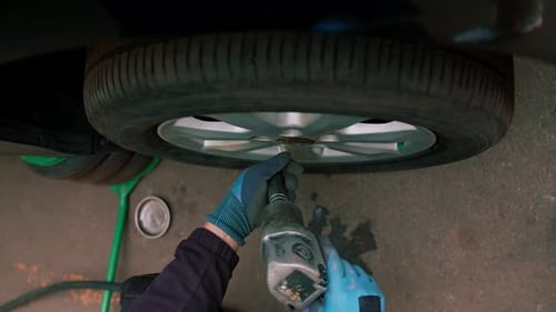 Auto mechanic changing a wheel from a black car using a drill in a tire shop on the street detailing