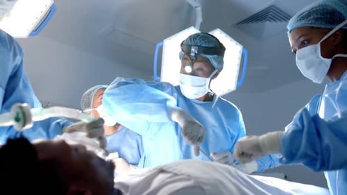 Diverse surgeons wearing surgical gowns operating on patient in operating theatre, slow motion