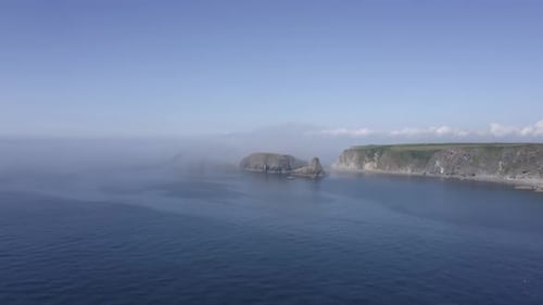 Ocean aerial along rugged coastal cliffs as fog rolls in off the sea