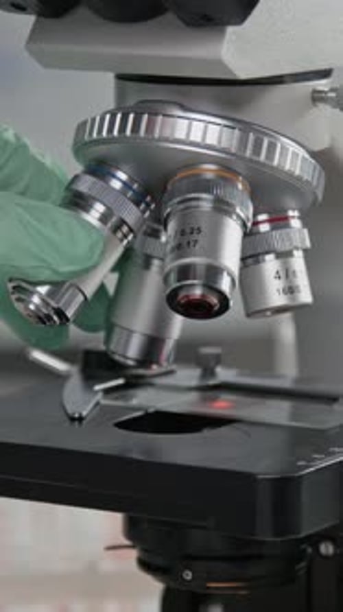 Gloved Hand Adjusting Microscope Lens for Scientific Research
