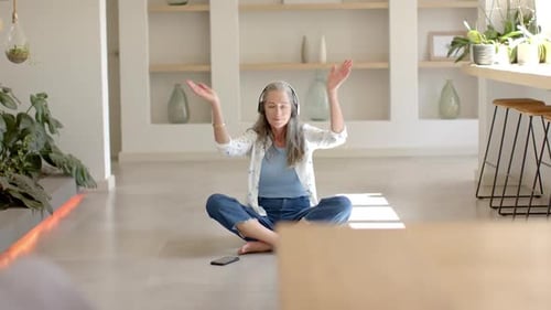 Mature Woman Meditating with Headphones in a Sunny Room