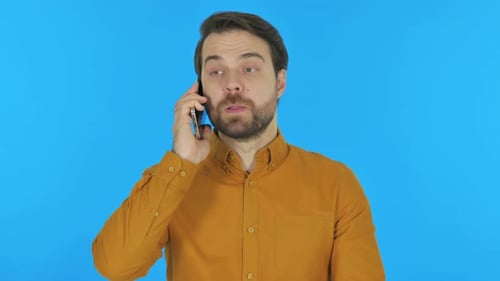 Angry Man Talking on Phone on Blue Background, Portrait