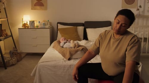 Young Mother Exercising on Fitness Ball and Smiling at Baby Son in Cocoon
